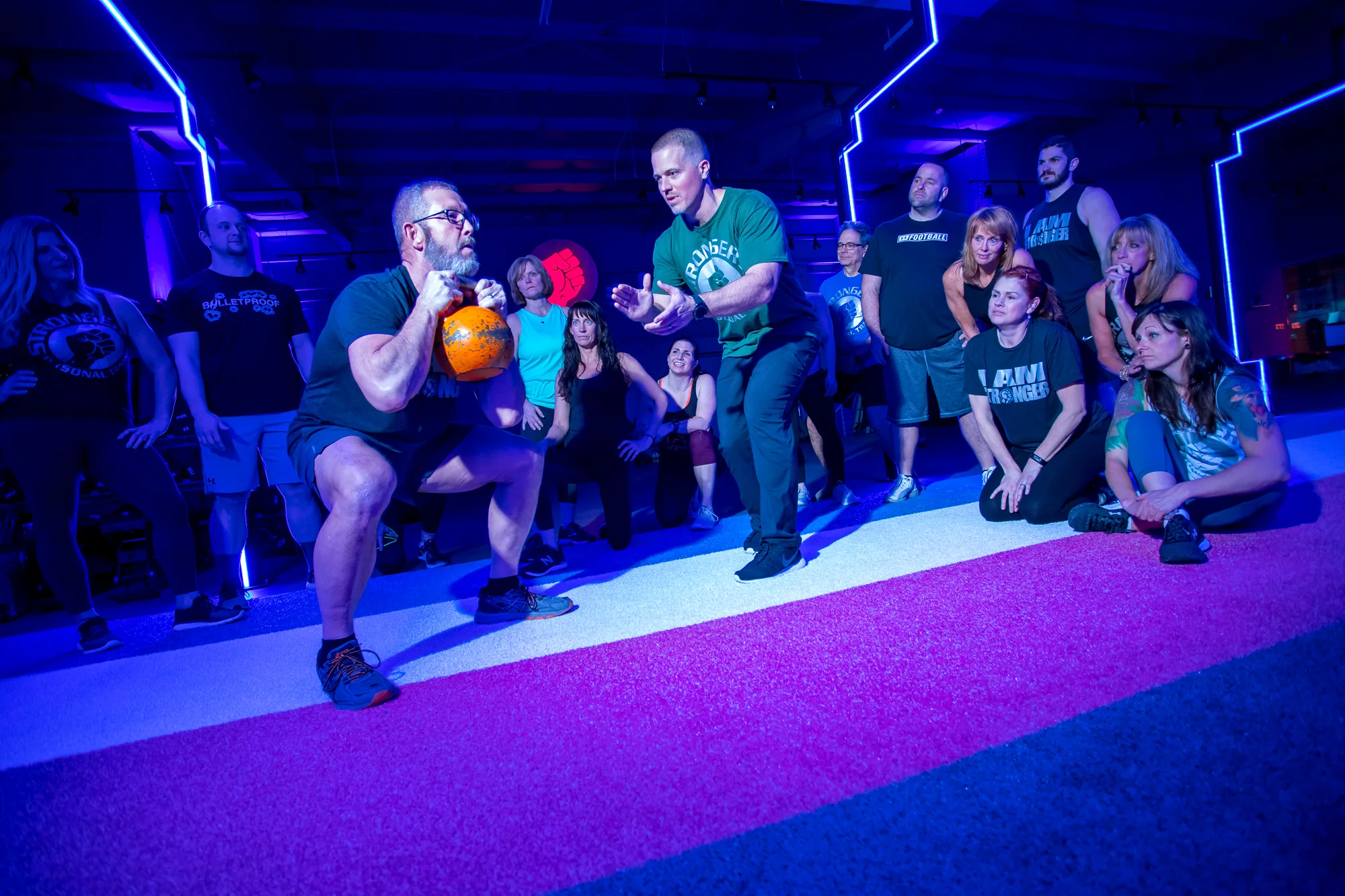 A member practising a kettlebell squat with a coach beside him.